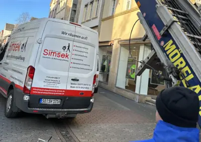 Transporter der Firma Simsek für Haushalts- und Wohnungsauflösungen in einer Stadtstraße, mit einem Kran im Einsatz.