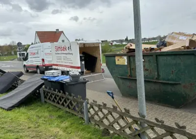 Transporter von Simsek Haushalts- & Wohnungsauflösung mit geöffnetem Heck, neben einem Container für Abfälle auf einer Straße.